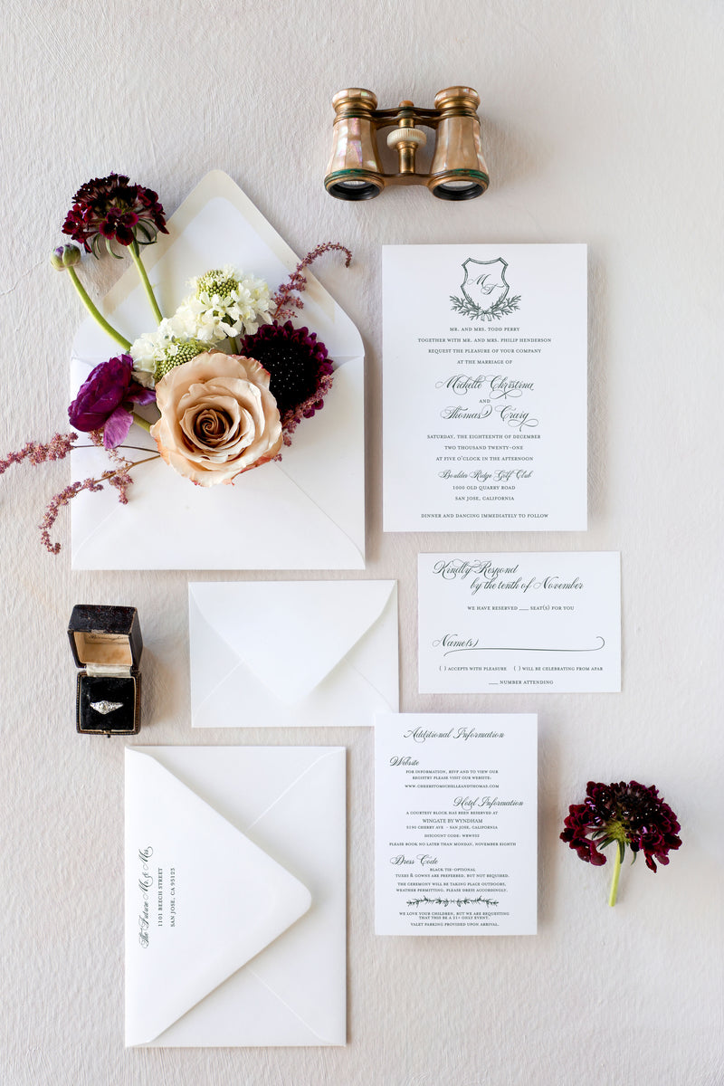 Winter wedding invitation suite with a monogram crest and wintergreen boughs and a small bow