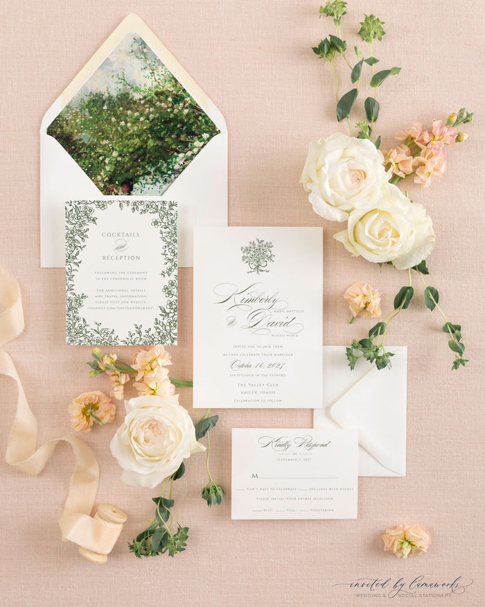 The Kim wedding invitation suite laid out with its hand-painted floral envelope liner, reception card, and invitation, surrounded by white roses and ribbon