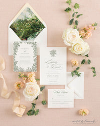 The Kim wedding invitation suite laid out with its hand-painted floral envelope liner, reception card, and invitation, surrounded by white roses and ribbon
