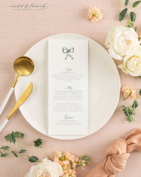 The Kim wedding menu card in sage green ink, plated with gold flatware and a knotted peach napkin