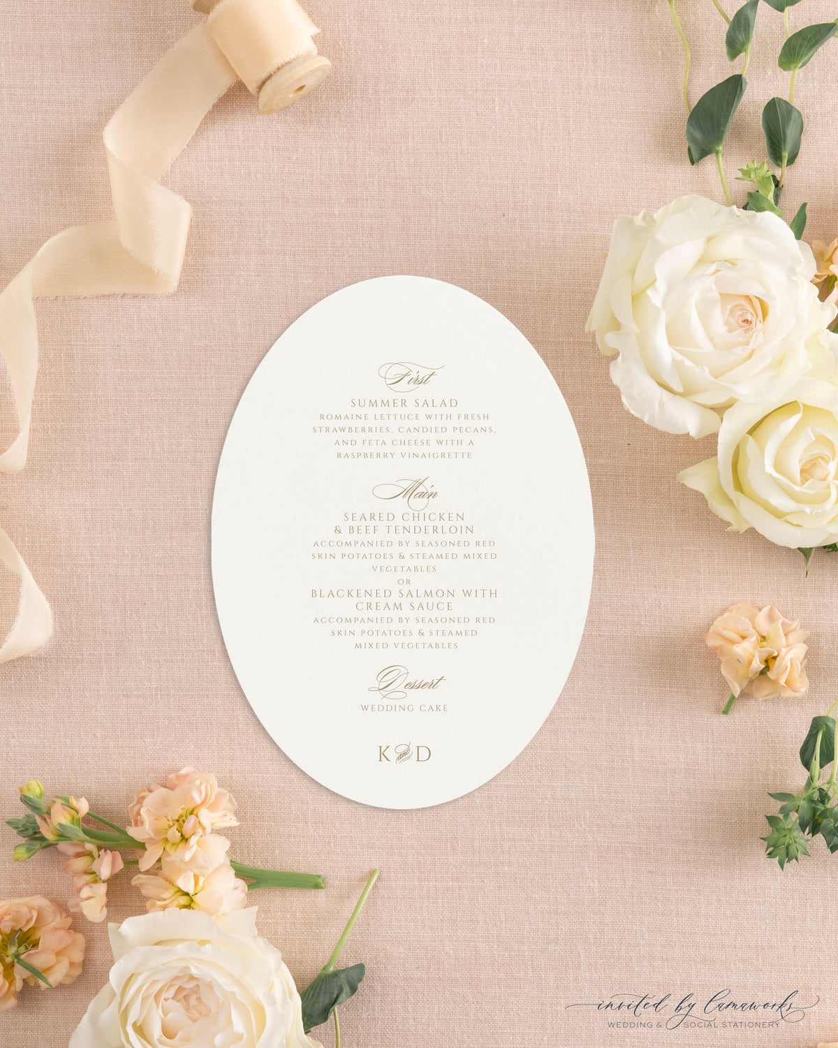The Kim collection oval die cut wedding menu card in gold ink with calligraphy course headers and a K and D monogram, styled with peach ribbon and roses